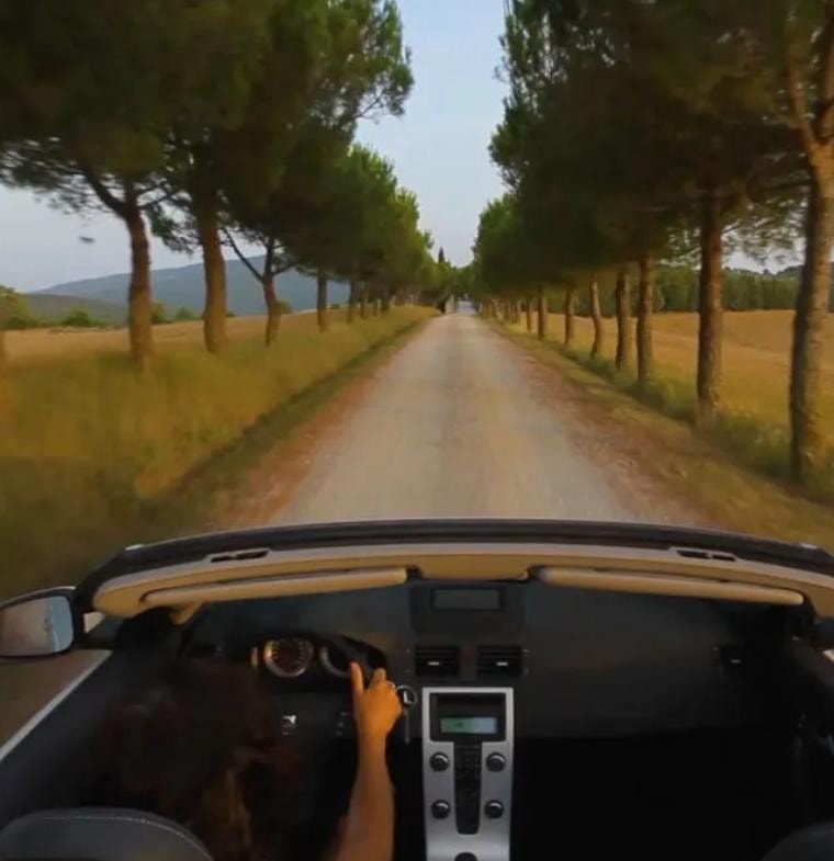Driving a convertible down a tree-lined Tuscan road